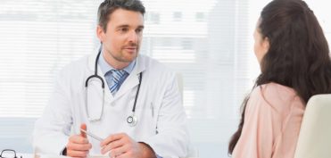 Male doctor listening to patient with concentration at desk in medical office